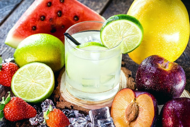 Copo de bebida típica brasileira chamada caipirinha, limão, álcool destilado, cachaça e açúcar. várias frutas ao redor