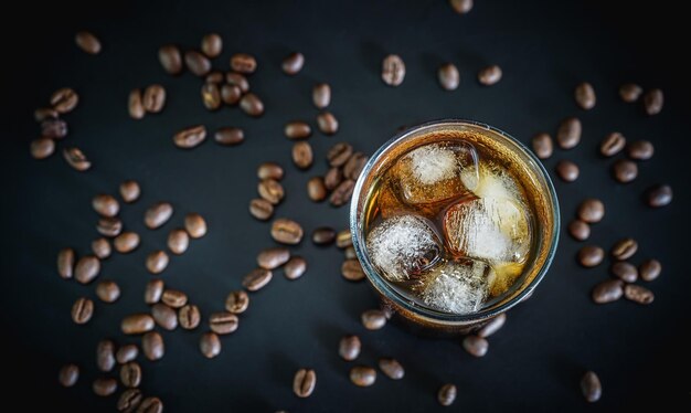 copo de café americano gelado em fundo preto com grãos de café torrados