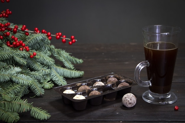 Copo de café, bombons de chocolate e galhos de árvores de natal e frutas vermelhas