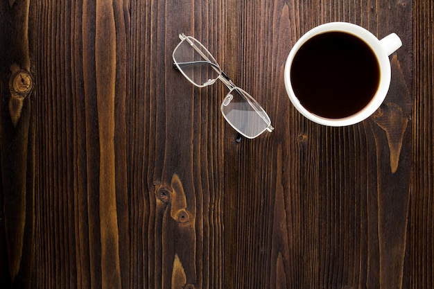 Copo de café branco com café preto e vidros na tabela de madeira.