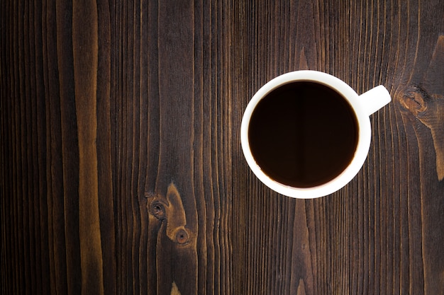 Copo de café branco com café preto na mesa de madeira.