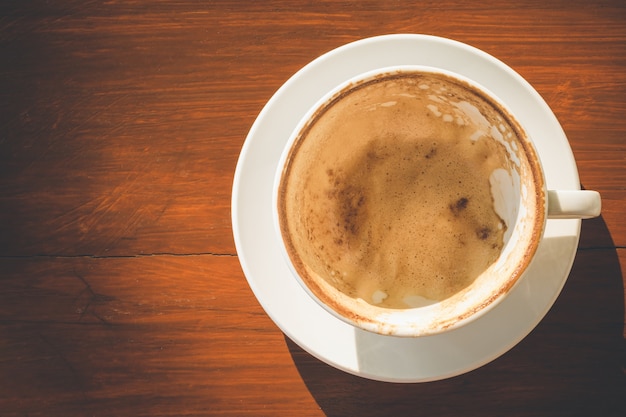 Copo de café branco vazio com espuma de café com leite depois de beber na mesa de madeira com espaço de cópia de texto ou desenho