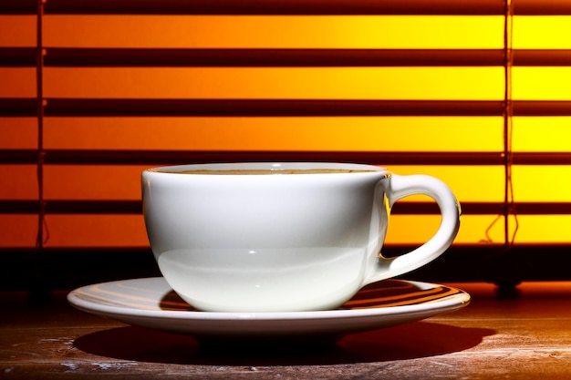 Copo de café cheio de café espumoso contra uma janela cega