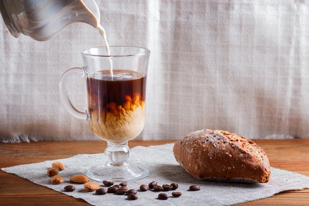 Copo de café com creme derramado e pão em uma madeira