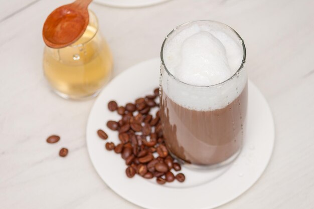 Copo de café com espuma de leite com mel na mesa de madeira branca.