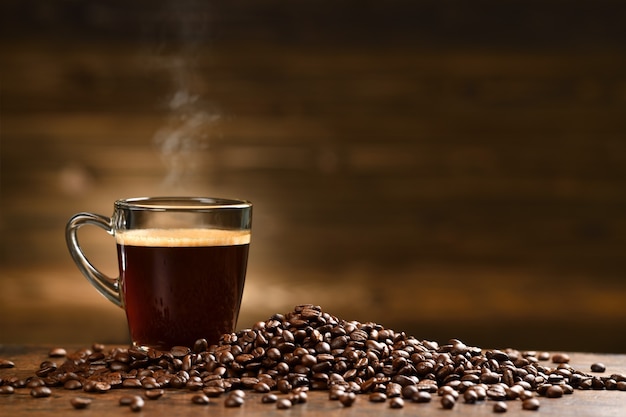 Copo de café com fumaça e grãos de café na velha mesa de madeira