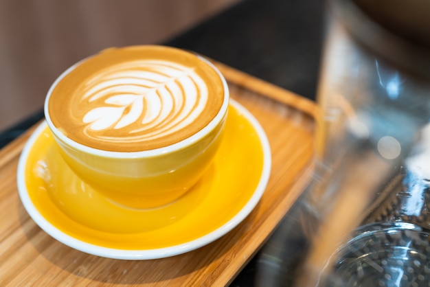 Copo de café de latte art em vidro amarelo na placa de madeira