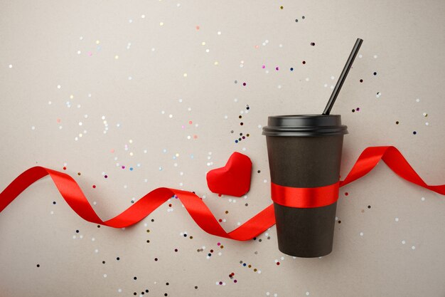 Copo de café de papel decorado com coração de origami vermelho, fita de seda e confetes