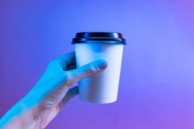 Copo de café de papel em uma mão em uma luz de neon na moda.