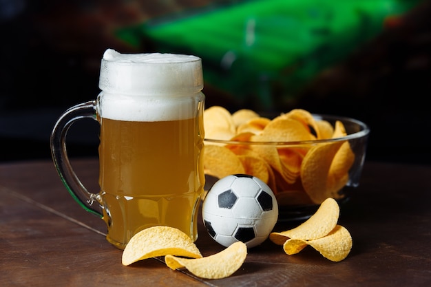 Copo de cerveja, bola de futebol e lanche em um jogo de futebol.