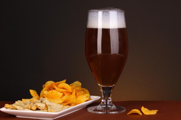 Copo de cerveja com bolachas e batatas fritas em fundo marrom