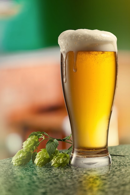 Copo de cerveja e lúpulo em uma mesa de madeira vazia contra um fundo verde natural