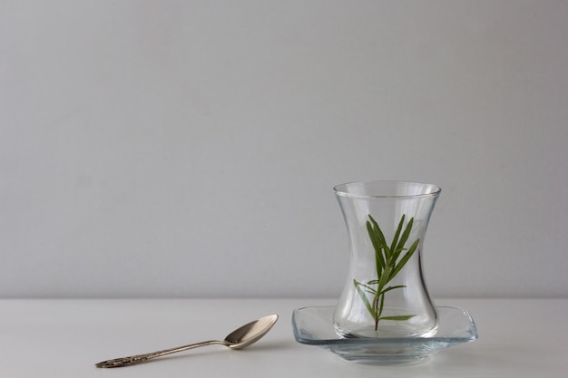 Copo de chá Armudu vazio com ramo de alecrim e colher sobre a mesa no fundo branco
