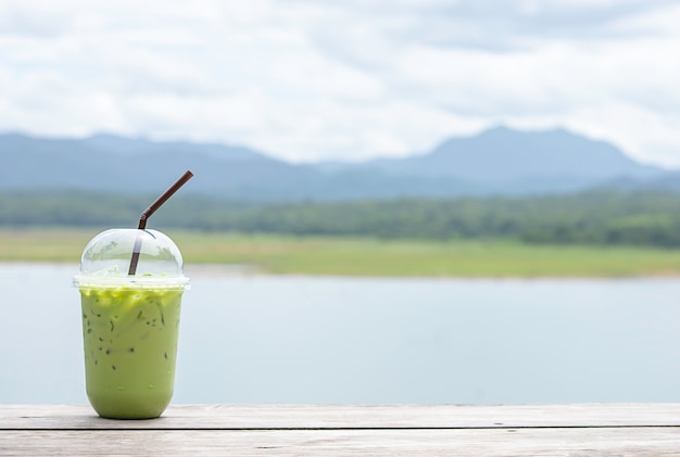 Copo de chá verde frio na mesa vistas embaçadas de fundo água e montanha.