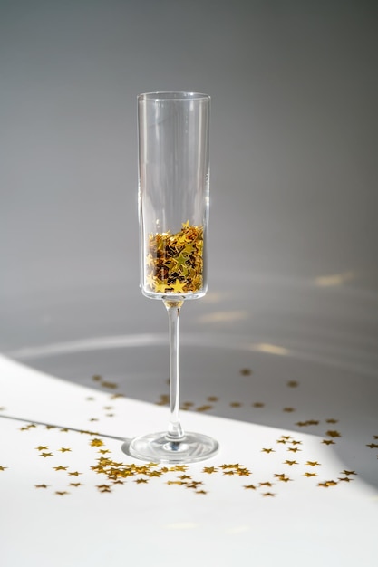 Copo de champanhe com confete dourado e espumante em fundo branco