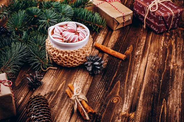 Copo de chocolate quente com marshmallows, canela, cones e ramos de abeto na mesa de madeira