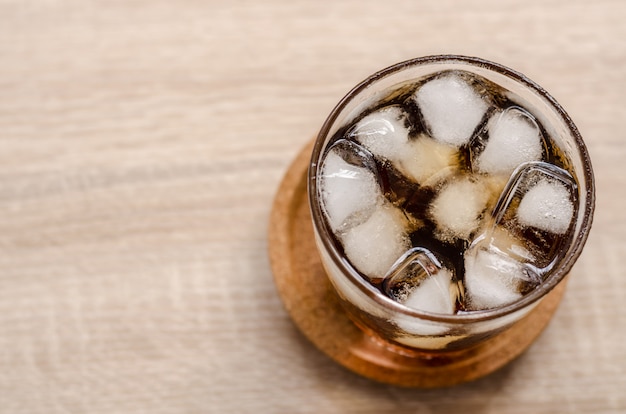 Copo de coca-cola com gelo no fundo de madeira