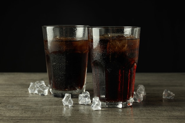 Copo de coca-cola e gelo na mesa texturizada cinza.