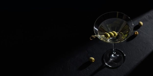 Copo de cocktail de martini seco clássico com azeitonas na mesa de pedra escura contra um fundo preto. Com espaço livre para o seu texto