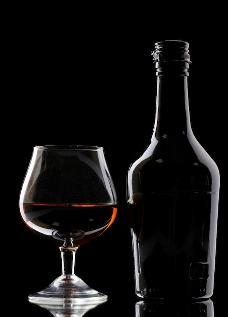 Copo de conhaque e garrafa em fundo preto