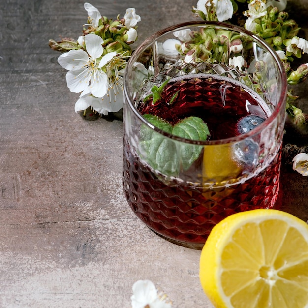 Copo de coquetel com cidra espumante de mirtilo ou limonada com mirtilos de limão fatiados e ramos de flor de hortelã acima de fundo de textura cinza Imagem quadrada