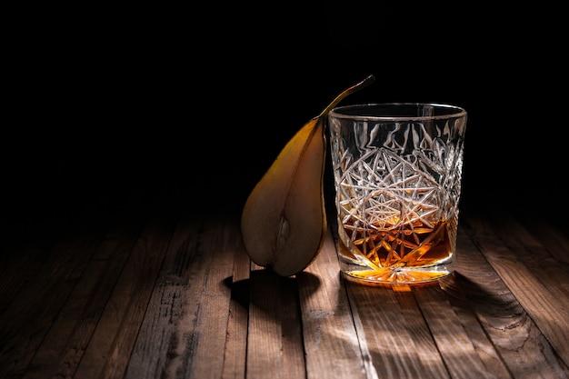 Copo de cristal com uísque e lanches em uma mesa de madeira em um fundo preto