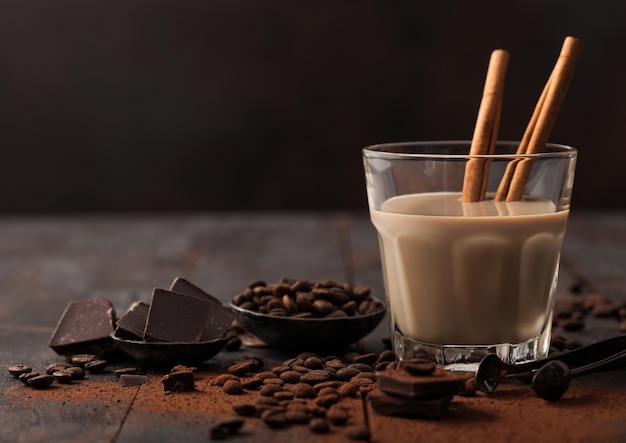 Copo de cristal de licor de baileys creme irlandês com grãos de café de canela e pó com chocolate escuro em fundo de madeira escura Espaço para texto