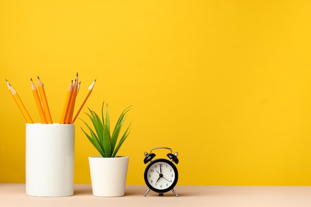 Copo de escritório com lápis e papelaria contra vista frontal de fundo amarelo