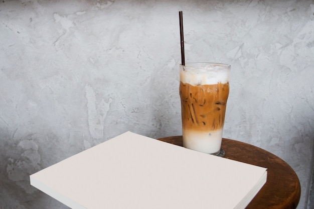 copo de gelo com leite com livro em branco ou revista na mesa de madeira no café.