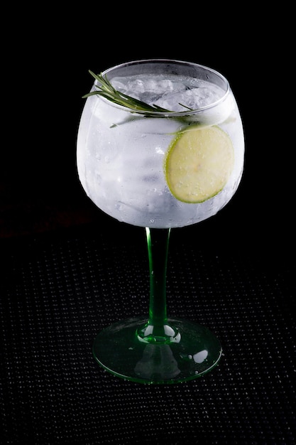 copo de gin e bebida tónica com limão e romário em fundo escuro em suporte de borracha