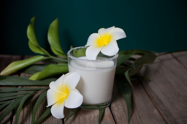 Copo de leite de coco com flores plumeria e folha de palmeira na madeira