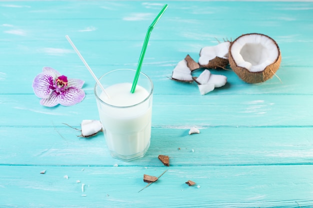 Copo de leite de coco na mesa de madeira azul. Decorado com coco e orquídea rosa na mesa de madeira. Foco seletivo