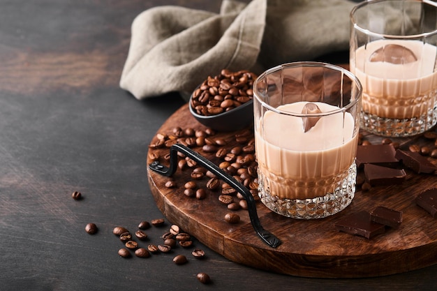 Copo de licor de baileys creme irlandês com grãos de café torrados, canela e chocolate na mesa de fundo de madeira escura. Foco seletivo.