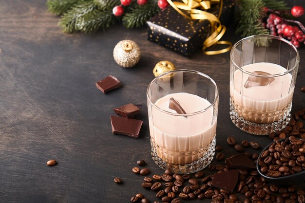 Copo de licor de baileys de creme irlandês com gelo, grãos de café torrados, canela, decoração de natal e chocolate na mesa de fundo de madeira escura. mesa de natal com presentes. foco seletivo.