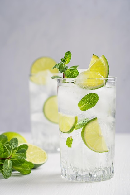 Copo de limonada fria, guarnecido com folhas de limão e hortelã, servido com gelo na mesa de madeira branca