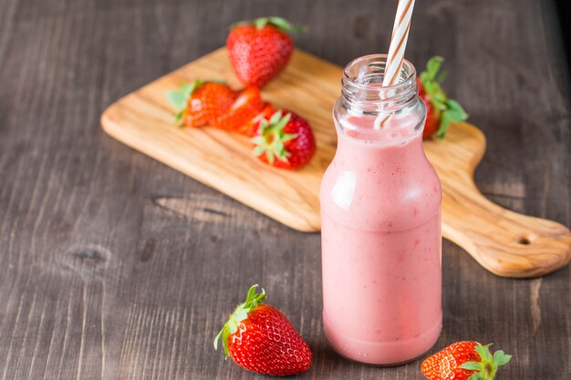 Copo de milkshake de morango fresco, batido e morangos frescos em fundo rosa, branco e madeira. Conceito de comida e bebida saudável.