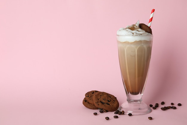 Copo de milkshake, sementes de café e biscoitos na parede rosa