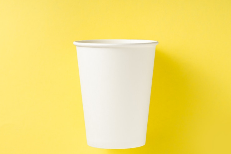Foto copo de papel branco sobre um fundo amarelo. vista superior. conceito de ecologia