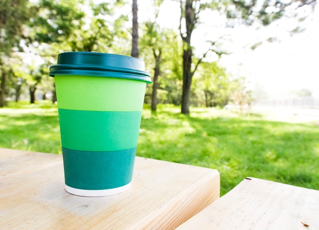 Copo de papel com bebida de café chá em uma mesa de vidro pertence à planta de fundo e uma parede verde. Conceito Zero West.