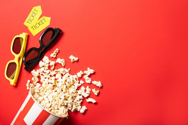 Copo de papel com pipoca em um fundo vermelho. Pontos e ingressos de cinema