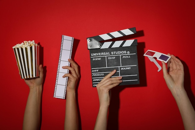 Copo de papel de clapperboard de filme de pipocas e óculos 3D nas mãos em fundo vermelho