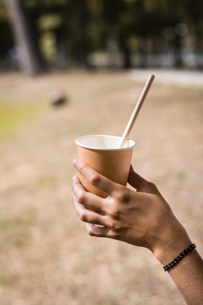 Copo de papel descartável com canudo na mão de um adolescente no parque em um dia quente