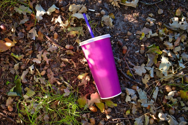 Copo de papel para refrigerante com tampa de plástico e canudo jogado no chão na floresta, copo de papel para milk-shake ou refrigerante na natureza, espaço em branco para o fundo do texto