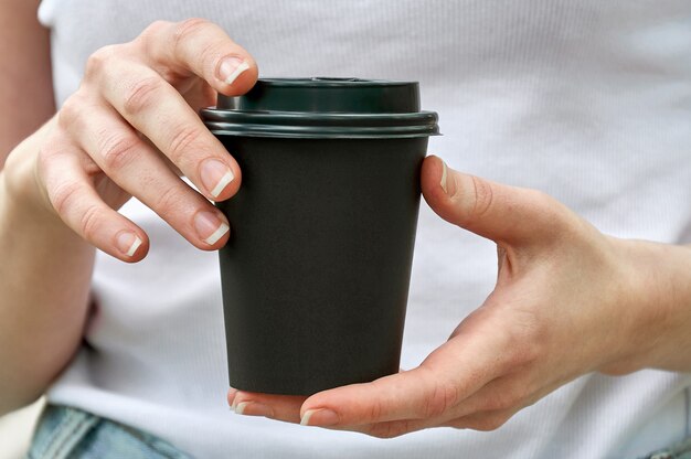 Copo de papel preto de close-up com café nas mãos da mulher. Brincar