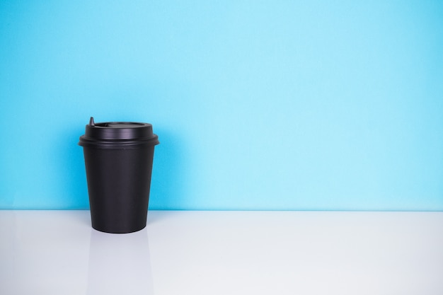 Copo de papel preto na mesa branca e fundo azul