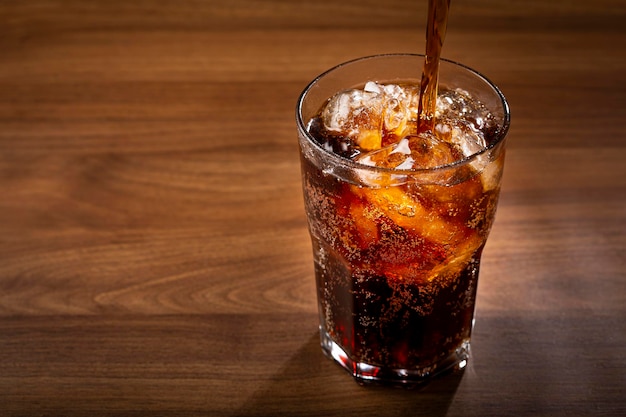 Copo de refrigerante de cola com cubos de gelo na mesa de madeira