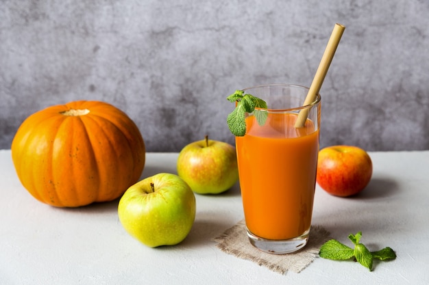 Copo de suco de abóbora decorado com folhas de hortelã e frutas com tubo de bebida em fundo cinza