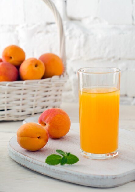 Copo de suco de damasco fresco e damascos maduros na cesta branca no fundo da parede de tijolo branco. Foco seletivo. Fechar-se.