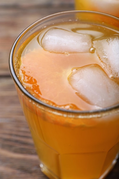 Copo de suco de laranja com bloco de gelo sobre fundo de madeira fechado