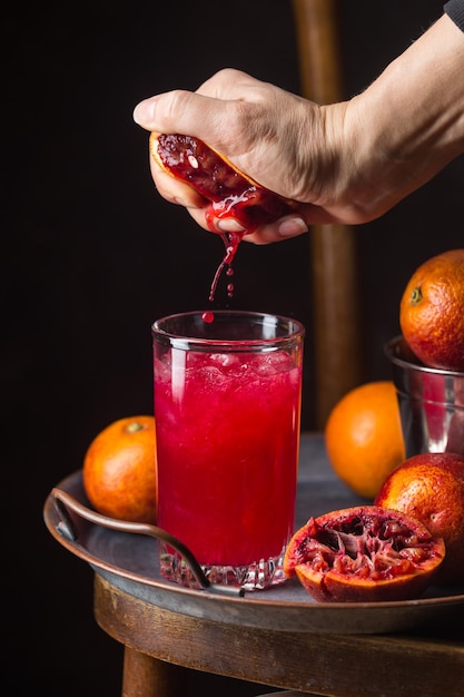 Copo de suco de laranja de sangue com gelo e frutas de laranja em fundo escuro